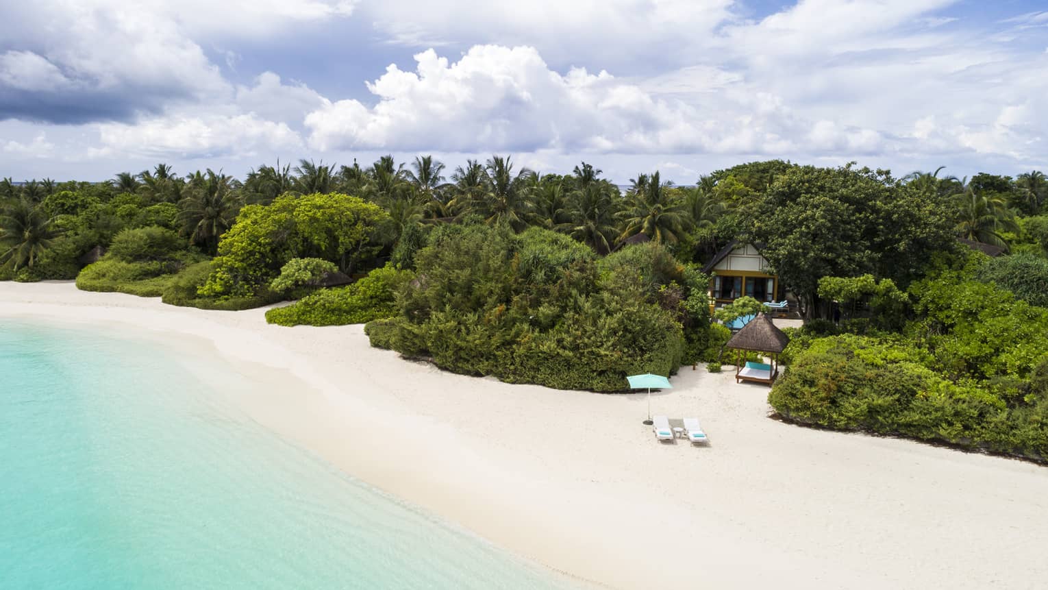 Quiet white-sand beach in the Maldives with turquoise water and lush green trees inland