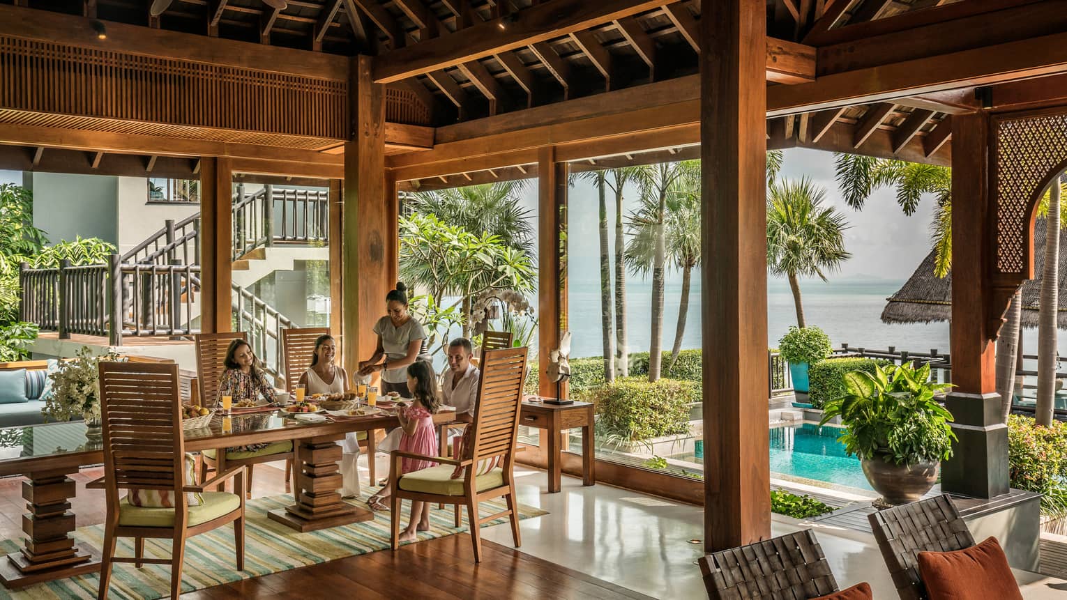 Butler serves family at long table in bright corner window dining room with windows