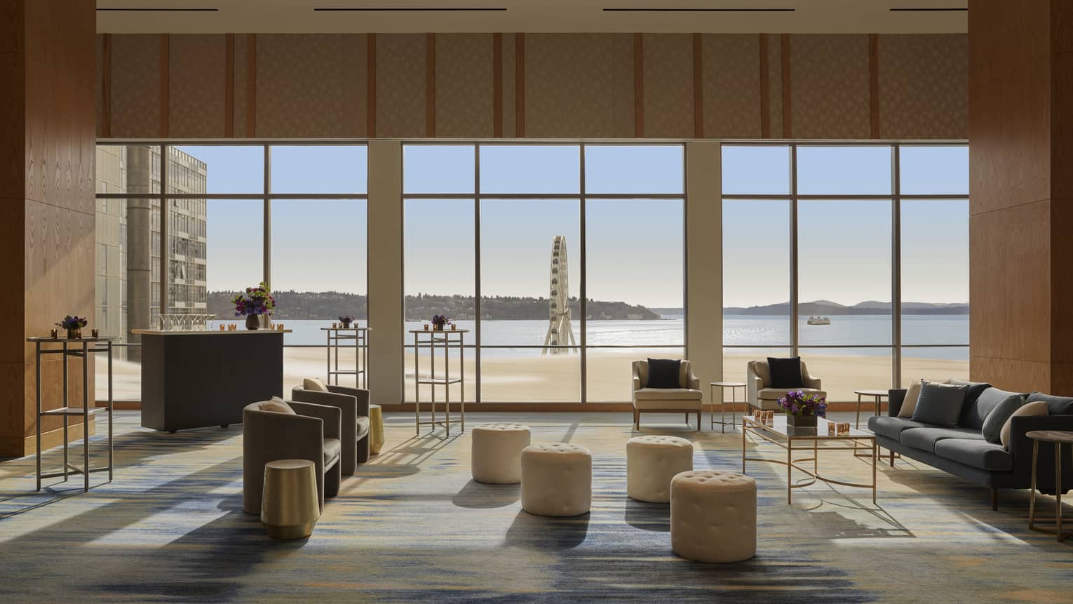 A large room with sofas, chairs, standing tables, stools and large windows.