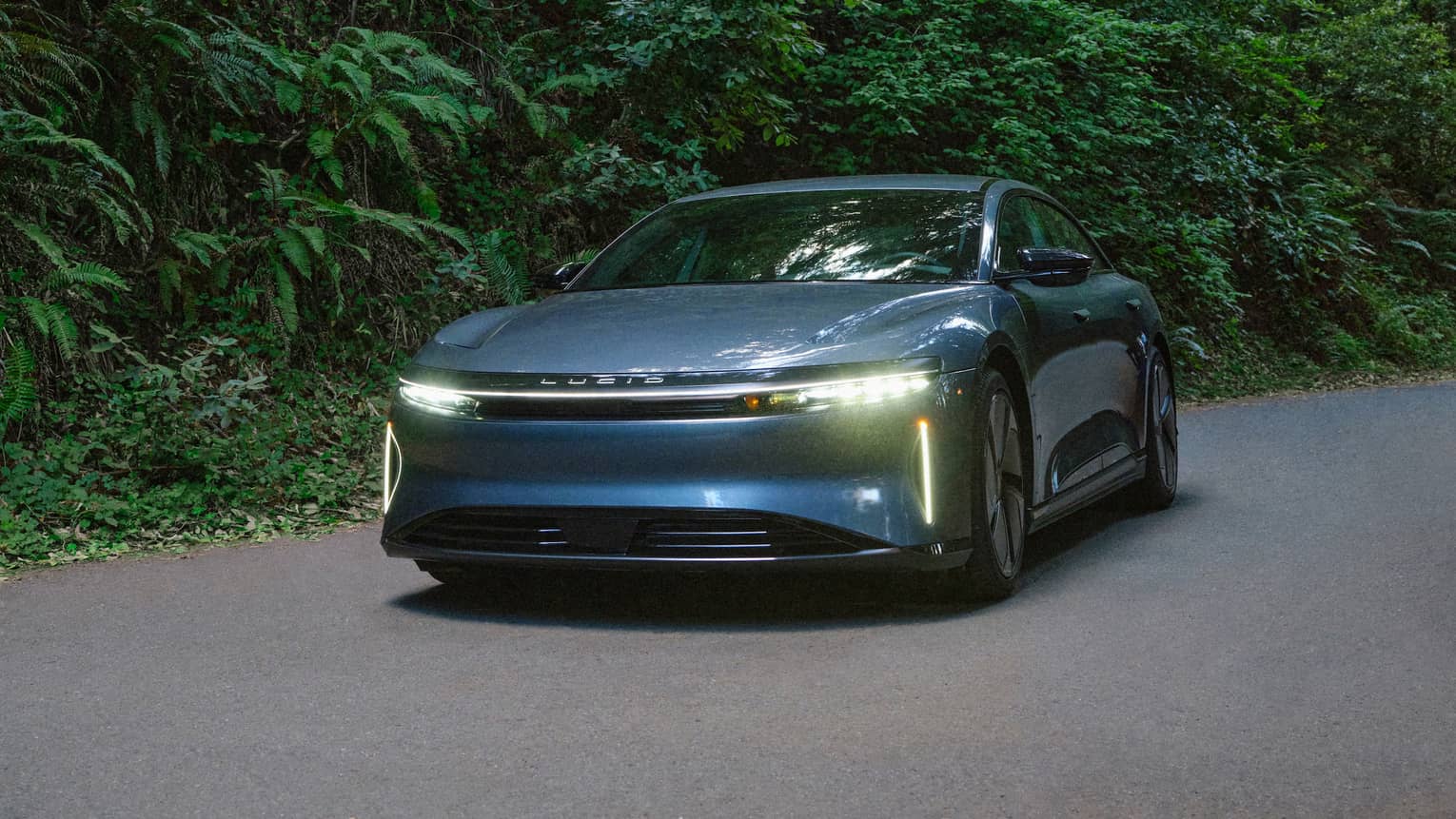 A car with the headlights on driving on a road near a forest