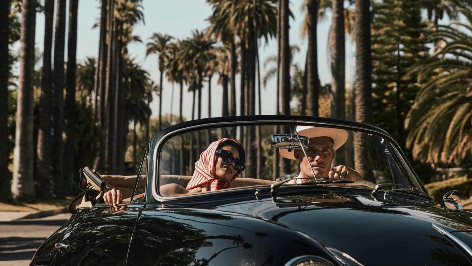 A couple drives down a palm tree?lined street in a black vintage convertible