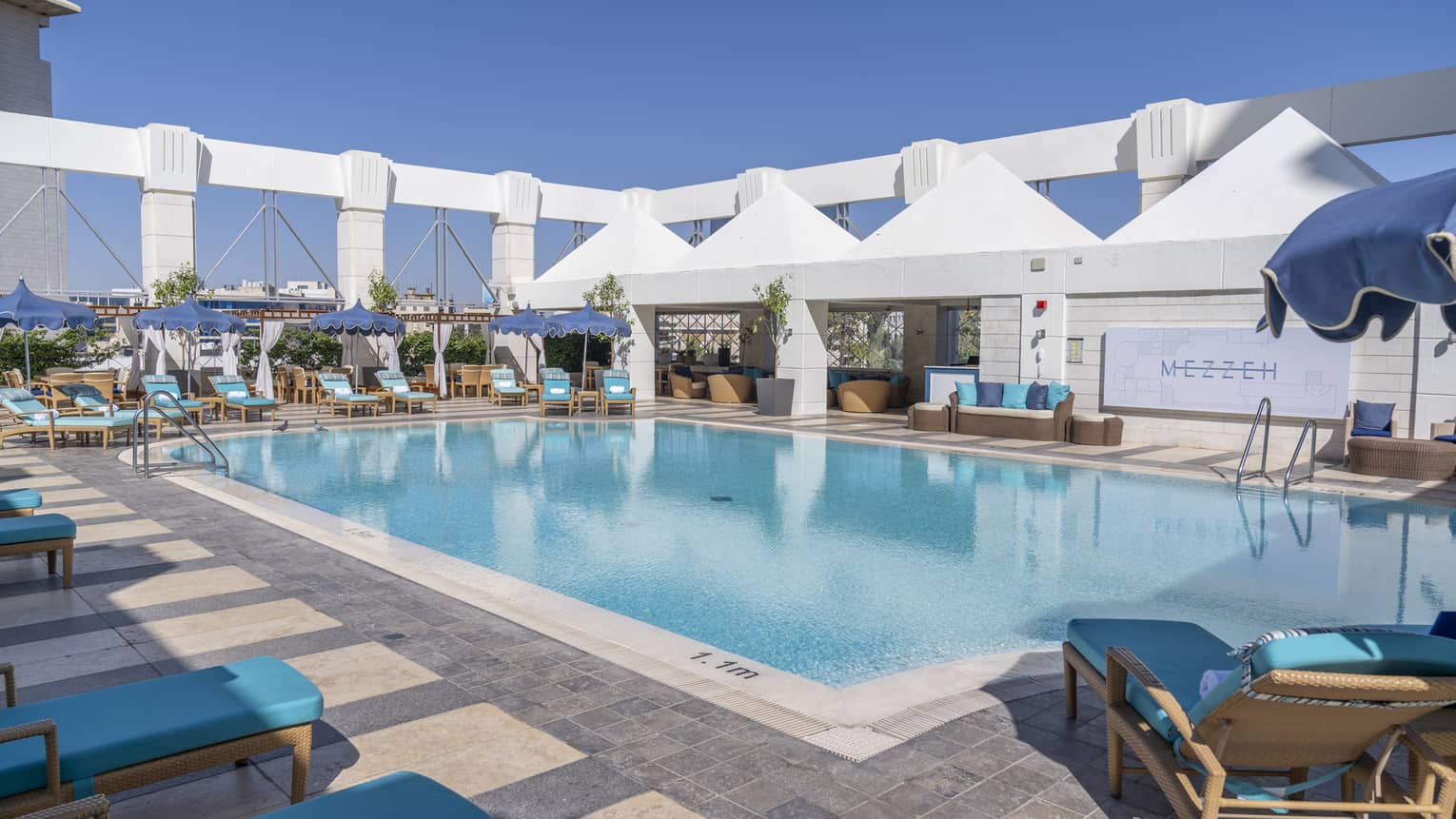 Outdoor pool surrounded by blue lounge chairs and four white tents