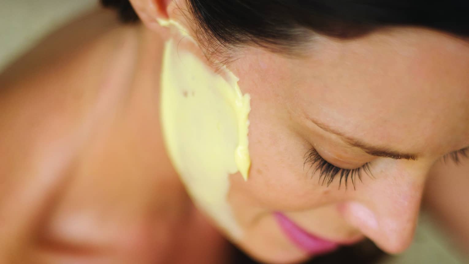 A close up of a woman looking down and smiling, with a yellow Sodashi Facial on her face