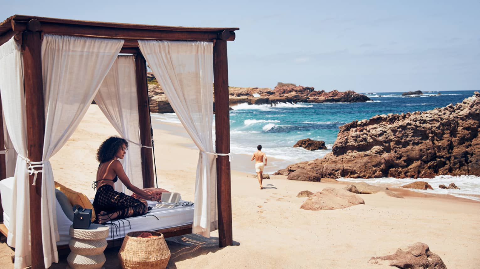 A woman on a small bed with a covering on a beach.