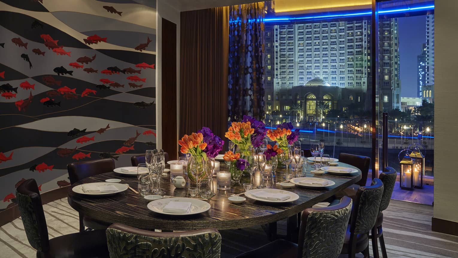 Private dining table with orange flowers in front of accent wall with fish print, window with city lights
