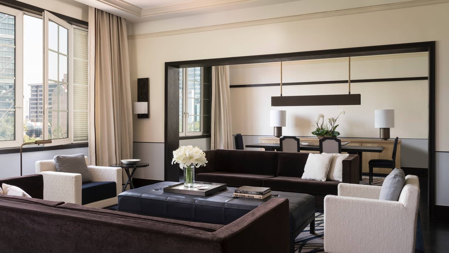 Presidential Suite bright living room with long sofas, white armchairs, tall sunny window, dining room