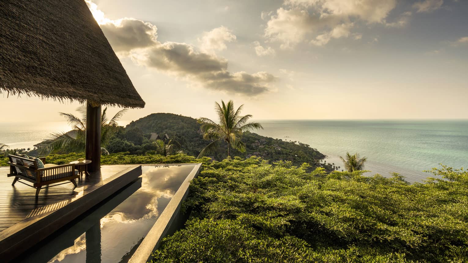 Patio lounge chair, thatched roof and deck overlooking canopy of tropical trees, ocean