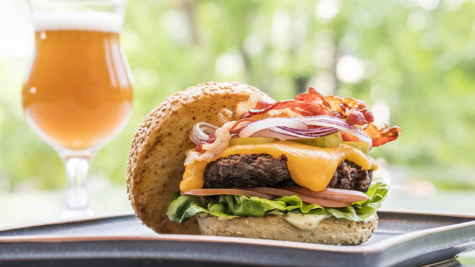 A burger with a glass of beer next to it.