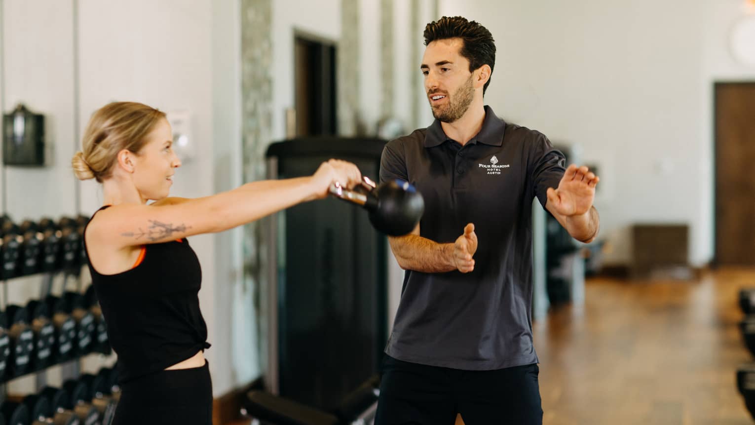 Male fitness trainer works with female guest who is using a kettlebell