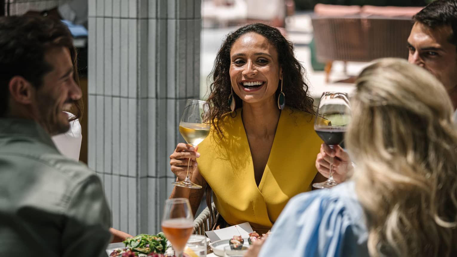 A group of guests hold glasses of wine while dining outdoors