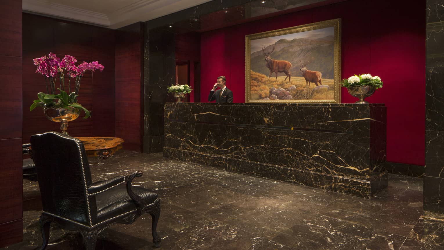Black marble floor, reception desk, staff answers phone under large painting of elk