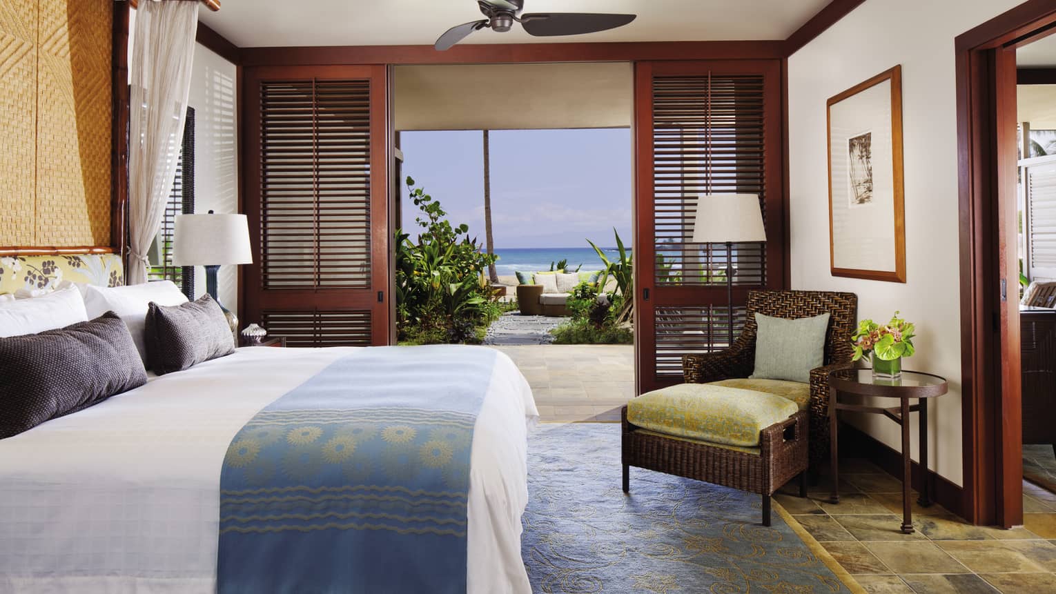 Superior Suite bed with blue-and-gold sash, wicker chair with gold velvet cushions by patio door