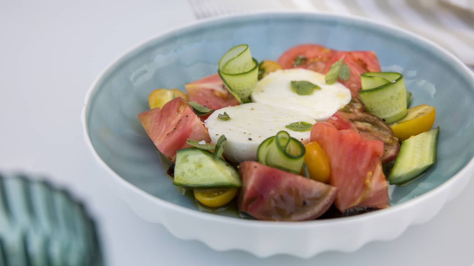 Heirloom tomato and buffalo mozzarella salad with shaved cucumber slices and figs served in a bowl