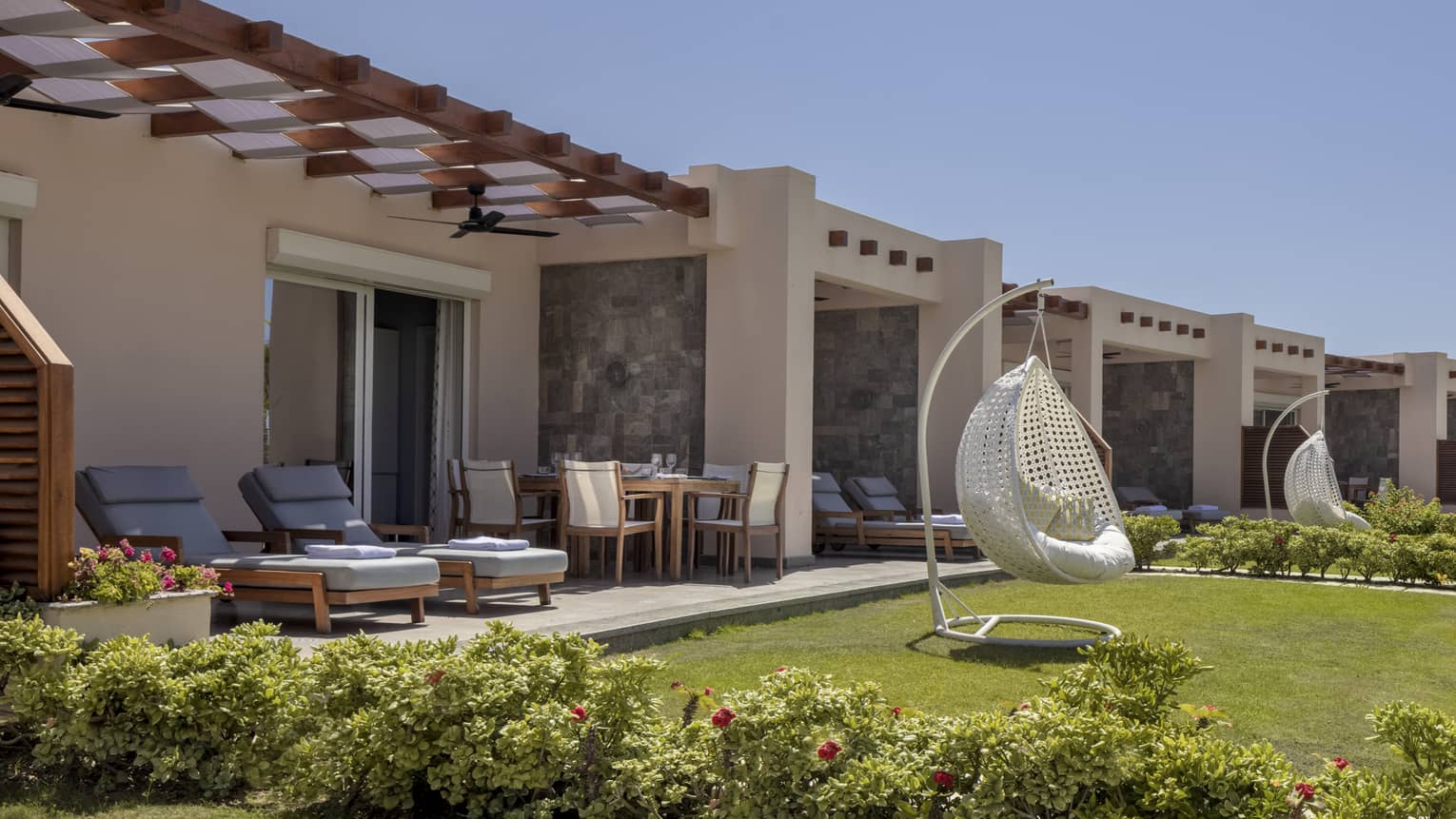 Suite patio and yard with blue lounge chairs and white egg chair, shrubbery