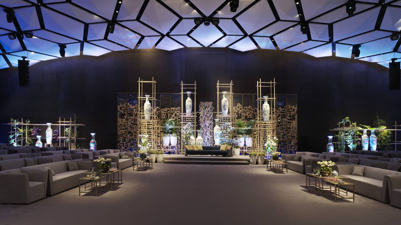 Darkly lit ballroom with couches to the side and modern floral display with large vases