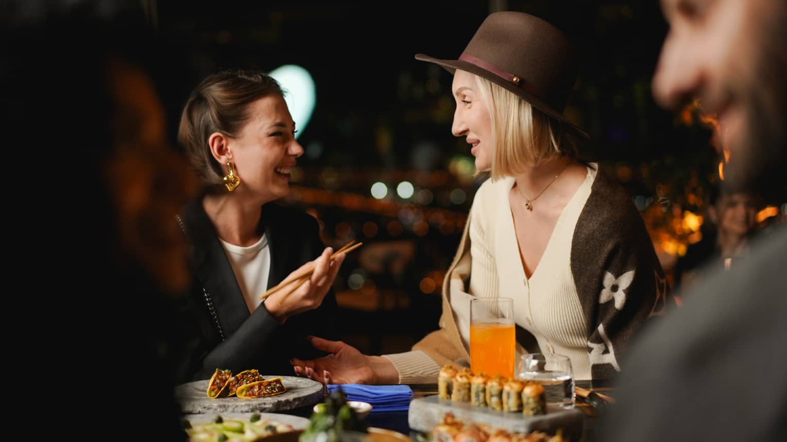 Two friends look at each other and smile as they sit at a dining table eating sushi