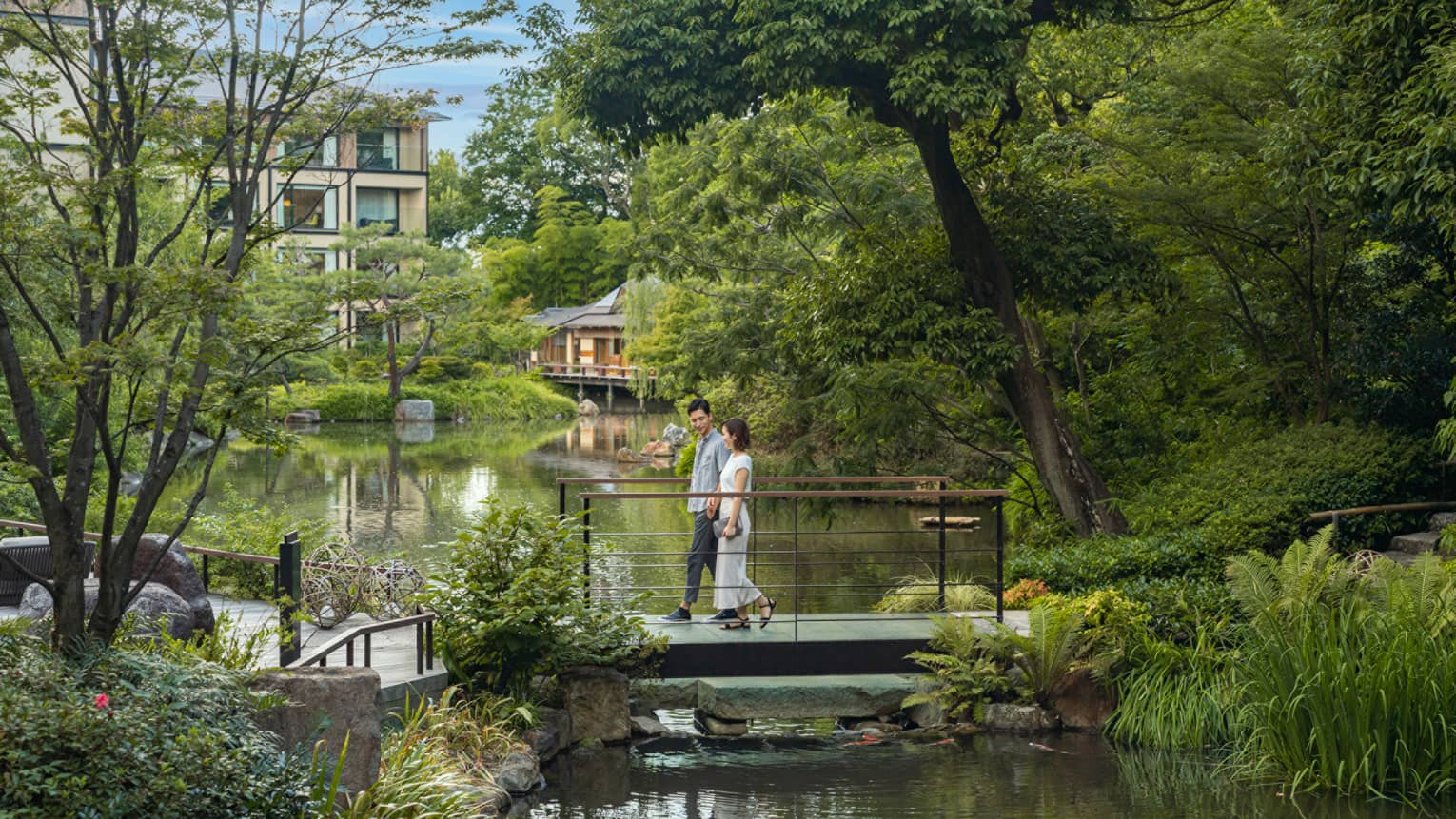 Couple walks across foot bridge over koi pond