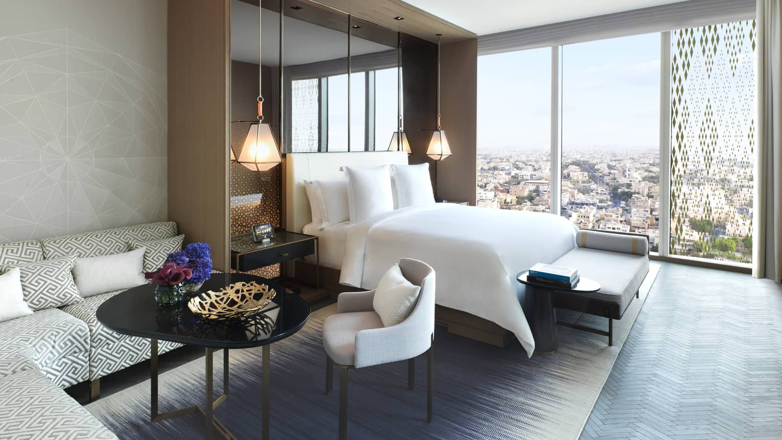 Hotel room L-shaped corner sofa, coffee table and chairs beside bed, wall of windows