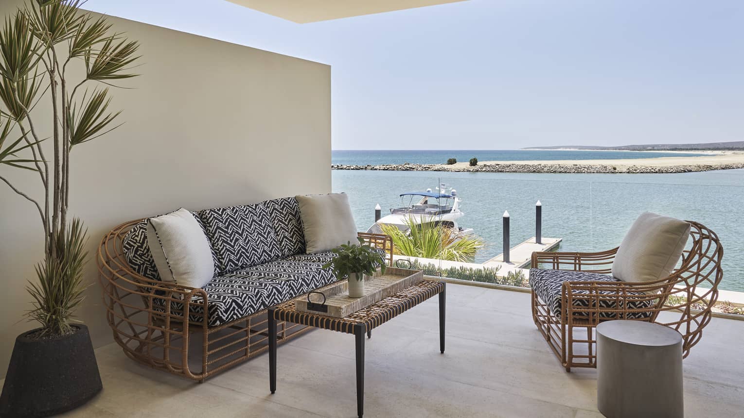Balcony with whicker sofa and chair, table, plant, marina view