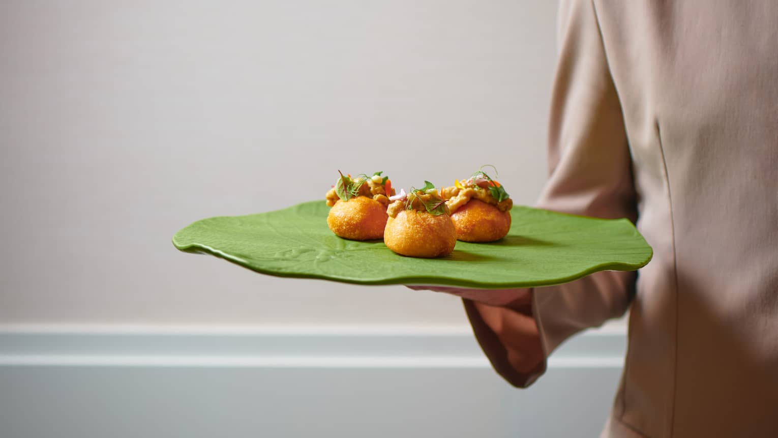 A person holding up a green platter with colourful hors d'oeuvres