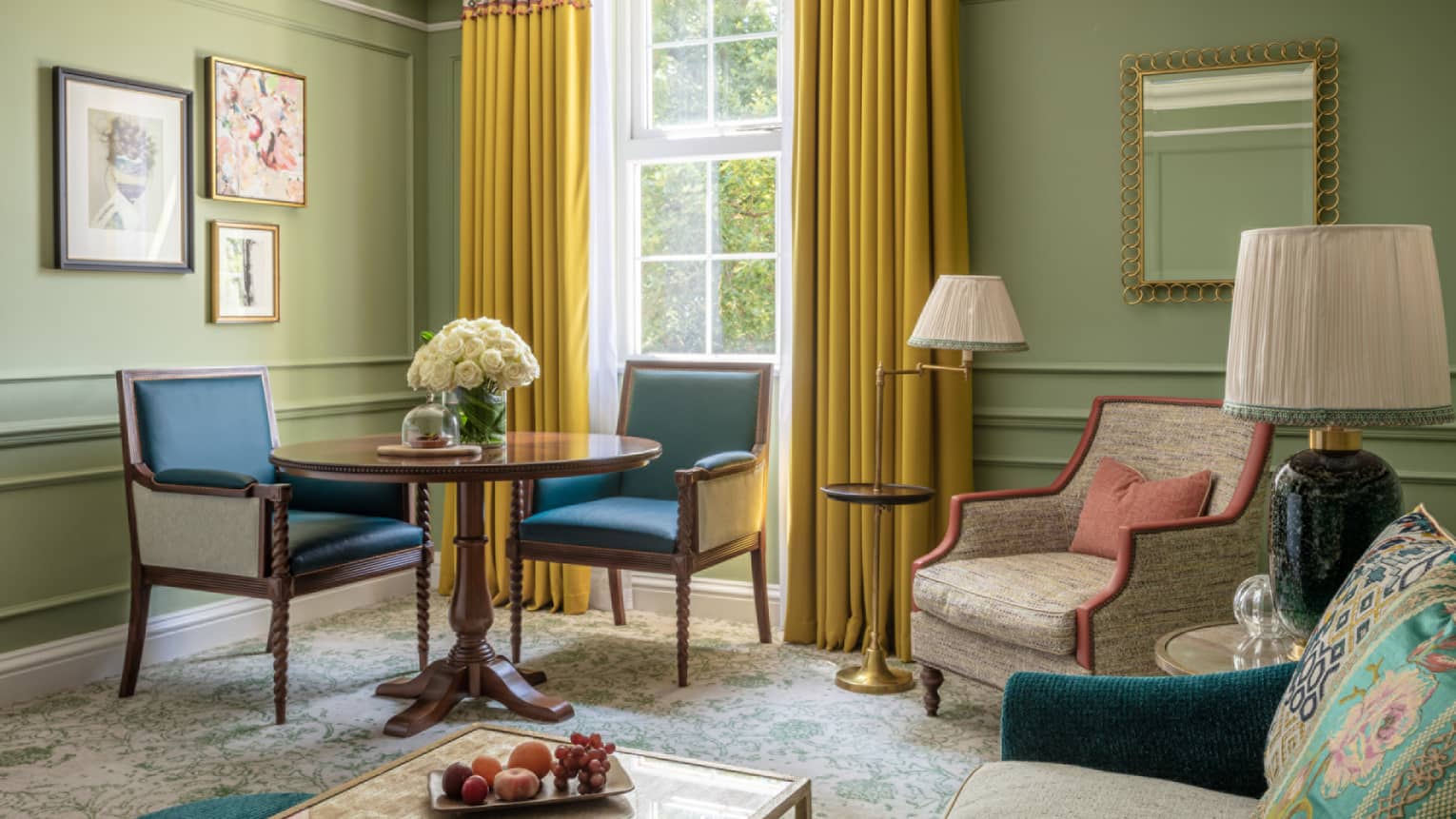 Guest room with cream accent chair, small round table with two leather dining chairs, avocado-coloured walls, window with yellow drapes
