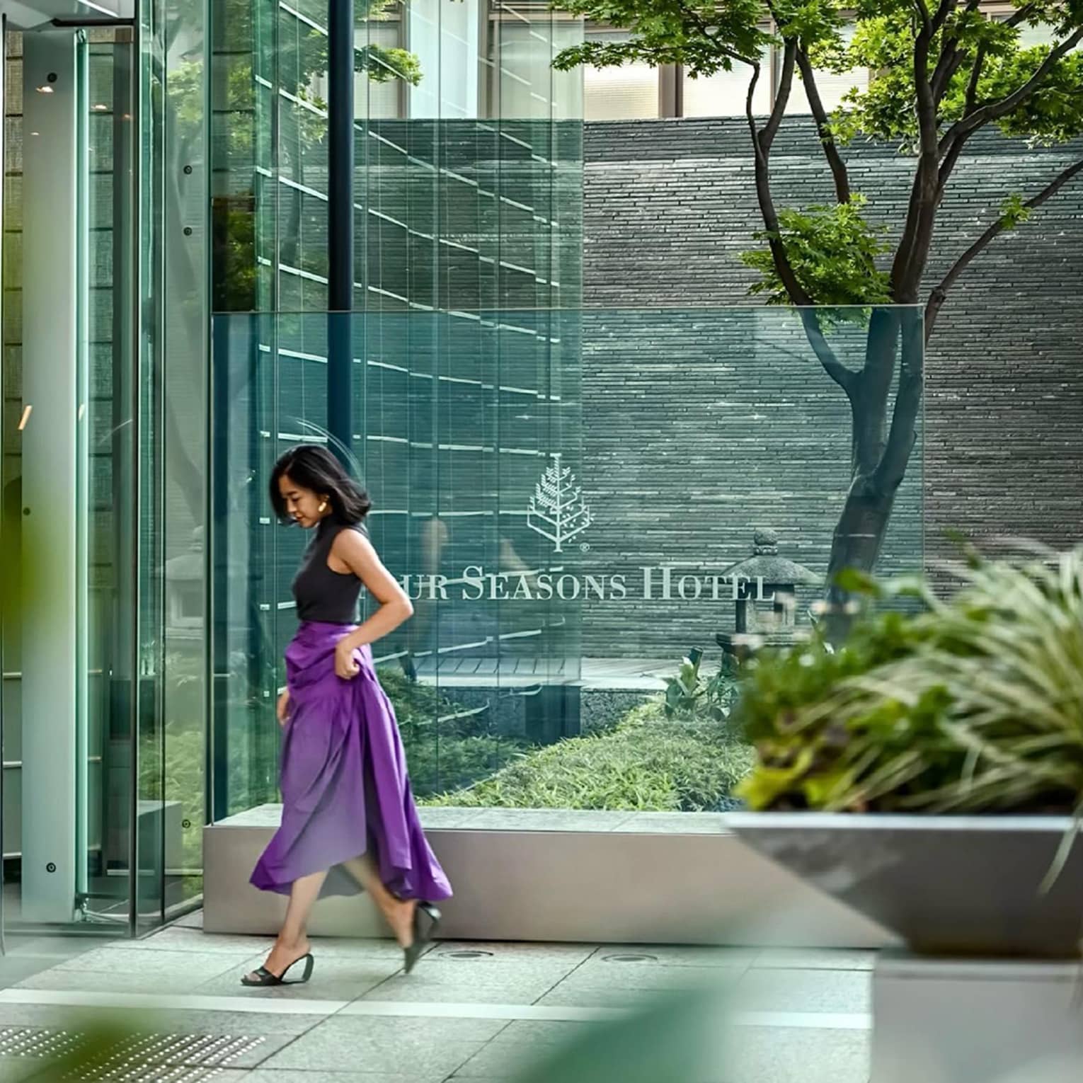 Person in a purple skirt walking past the glass entrance of Four Seasons 