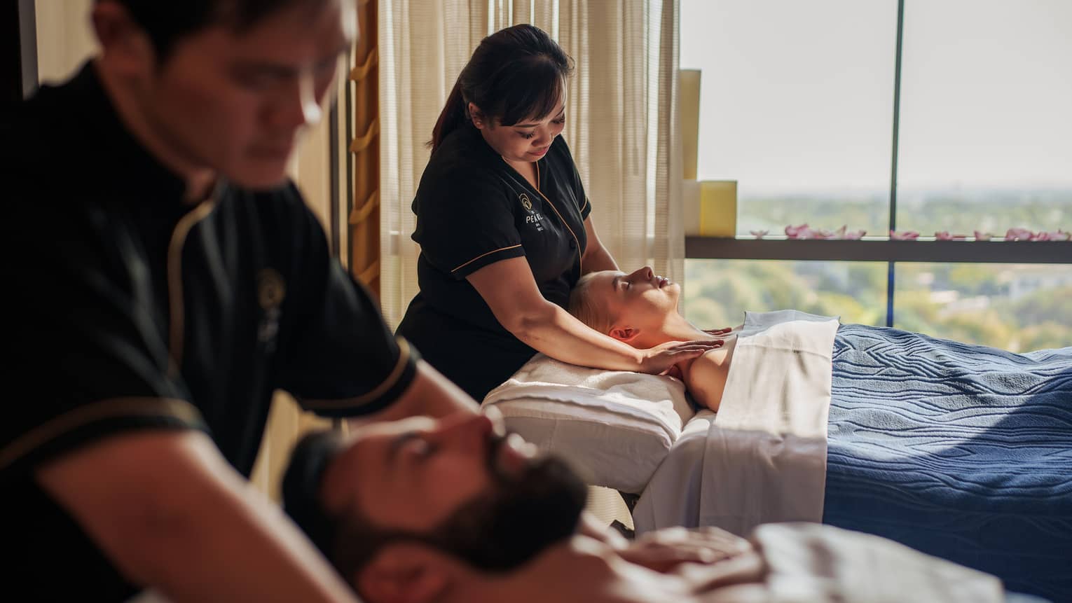 A couple gets massaged next to each other in a light-filled spa suite