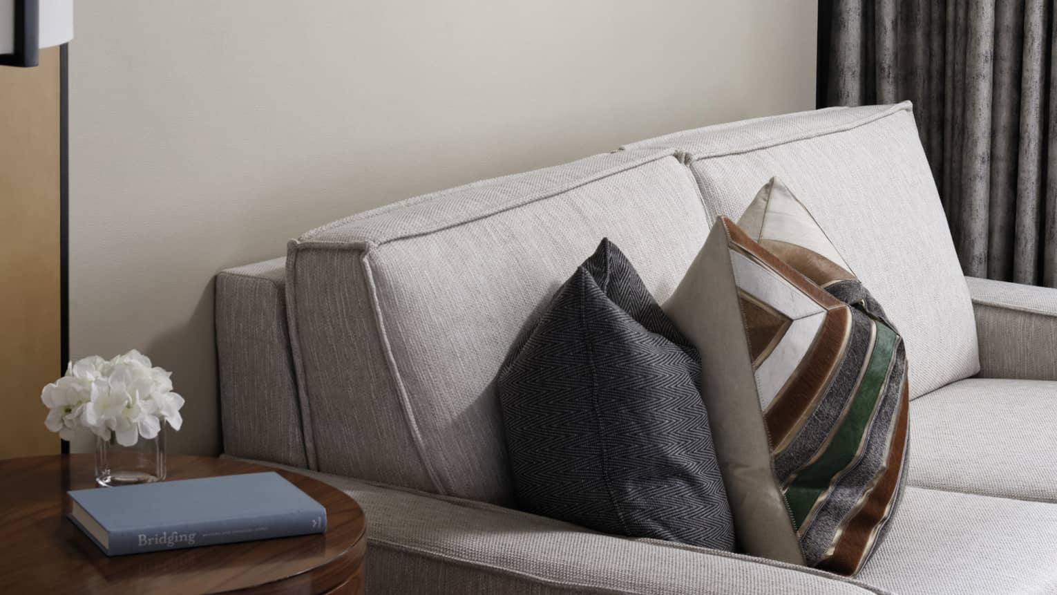 Cream loveseat, patterned accent pillows, wooden side table, wall art trio, grey curtains