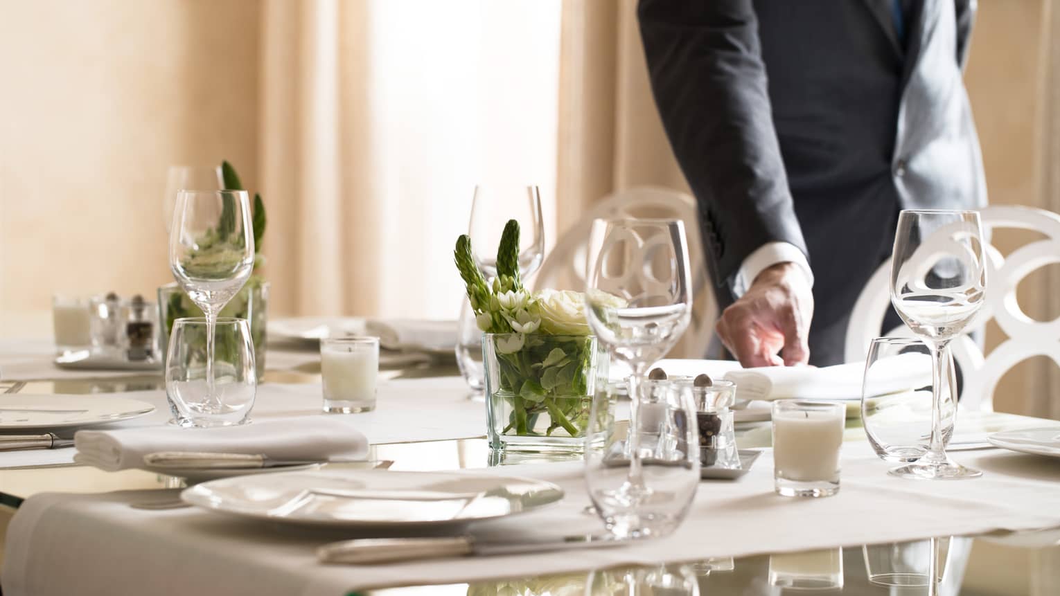 Hotel staff places napkin on small, elegant dining table in sunny room