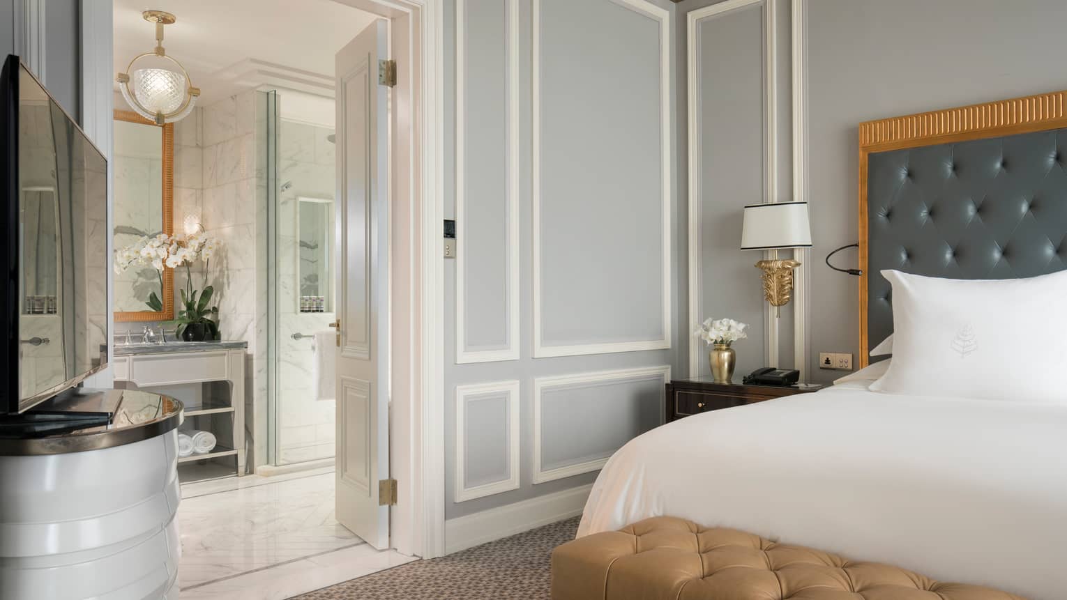 Executive Deluxe Suite corner of king-size bed with white linens, open door to bright bathroom