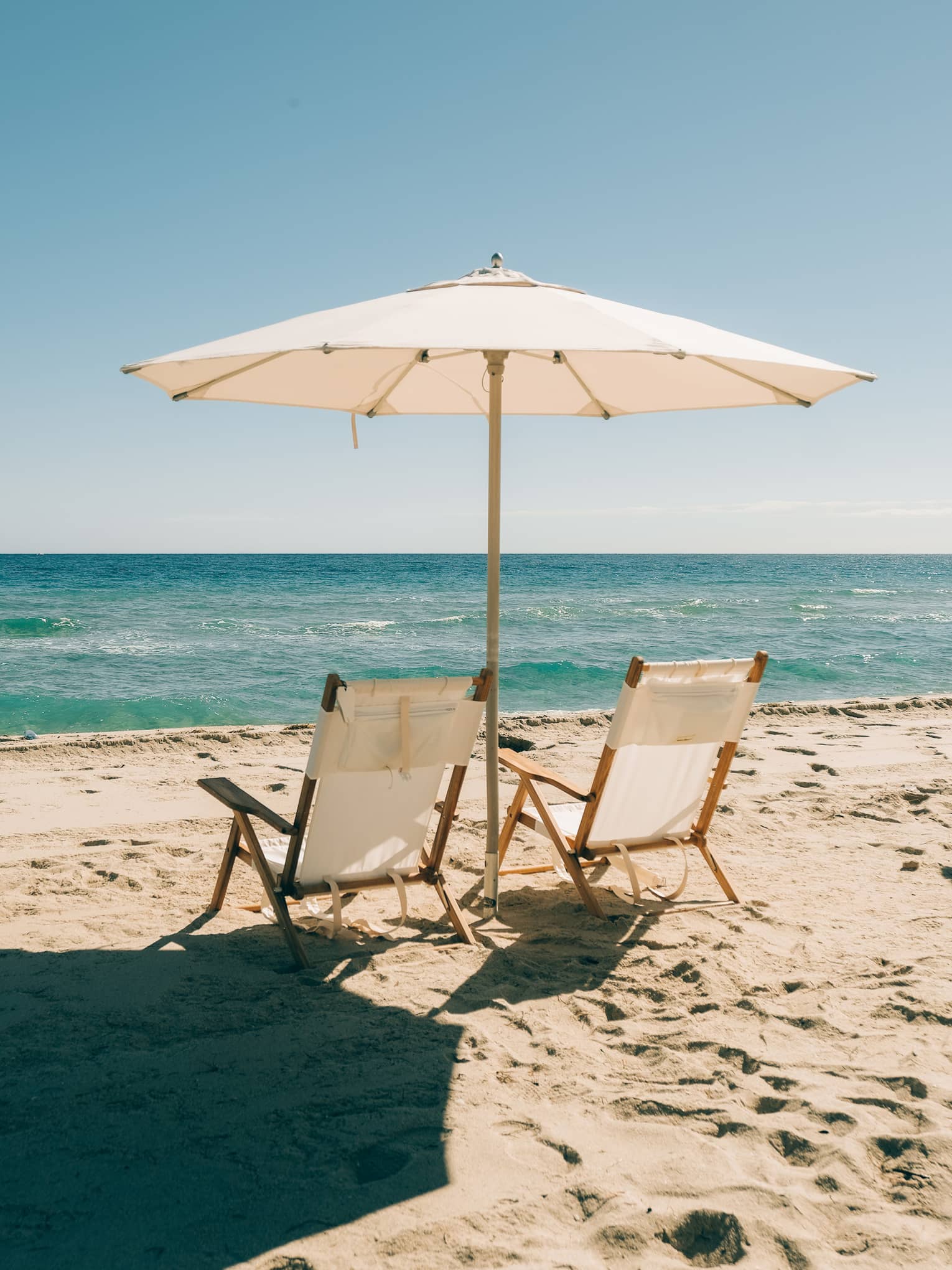 Two white beach chairs set up beneath a white umbrella on the sand