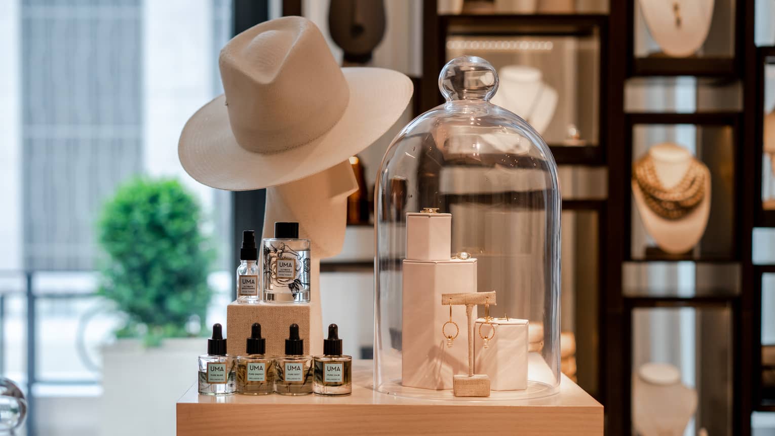 A boutique display of gold jewelry, a beige wide-brimmed hat, and wellness skin care products