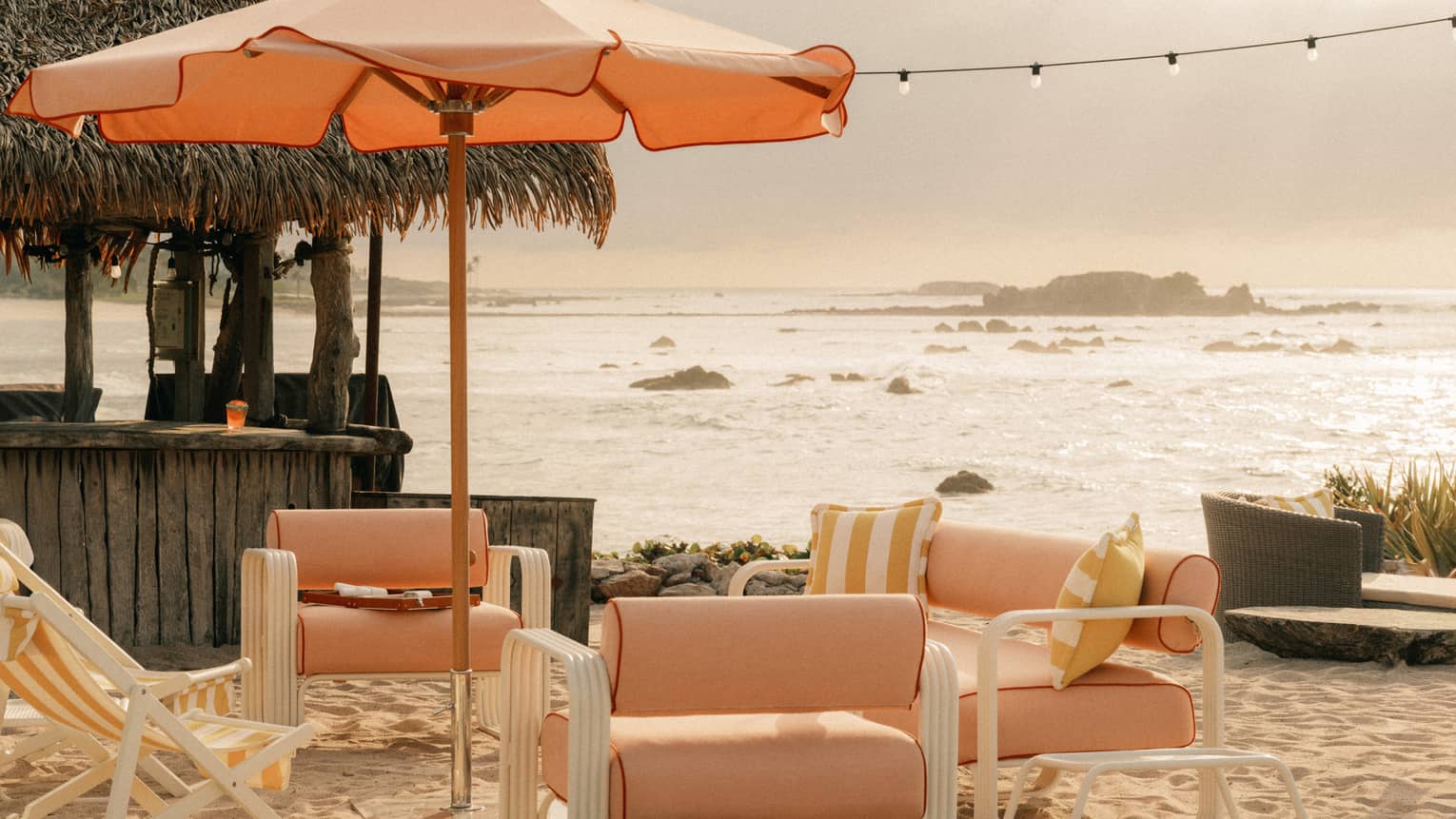 Light orange upholstered and fabric lounge chairs and sun umbrella on a beach with ocean and coastal views in the background