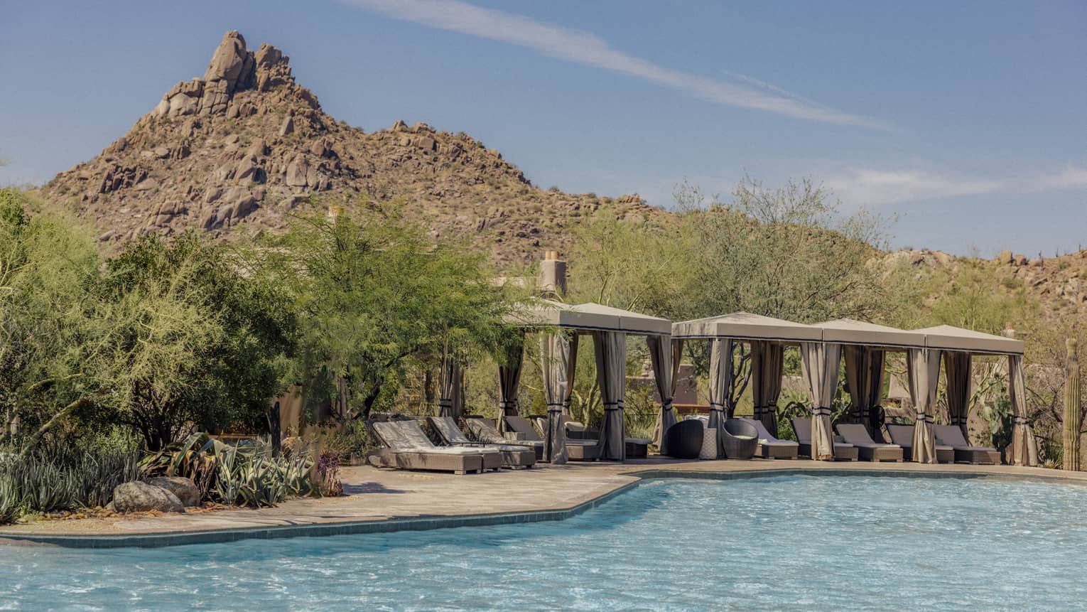 Pool with cabanas that have lounge chairs with a backdrop of the mountains.