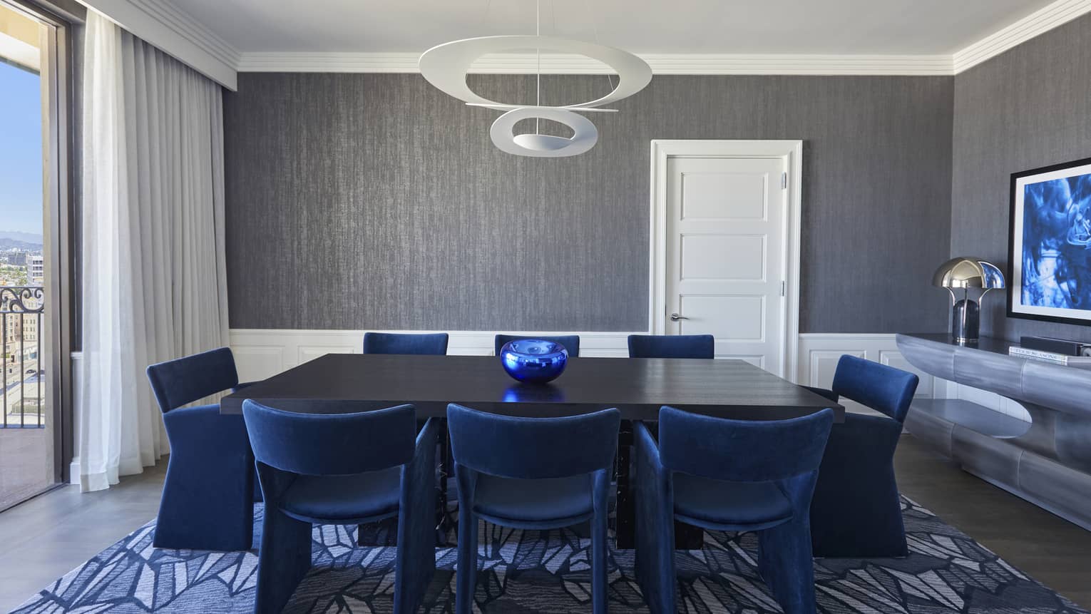 Dining room with black table and royal blue chairs, grey walls, blue carpet and floor-length window