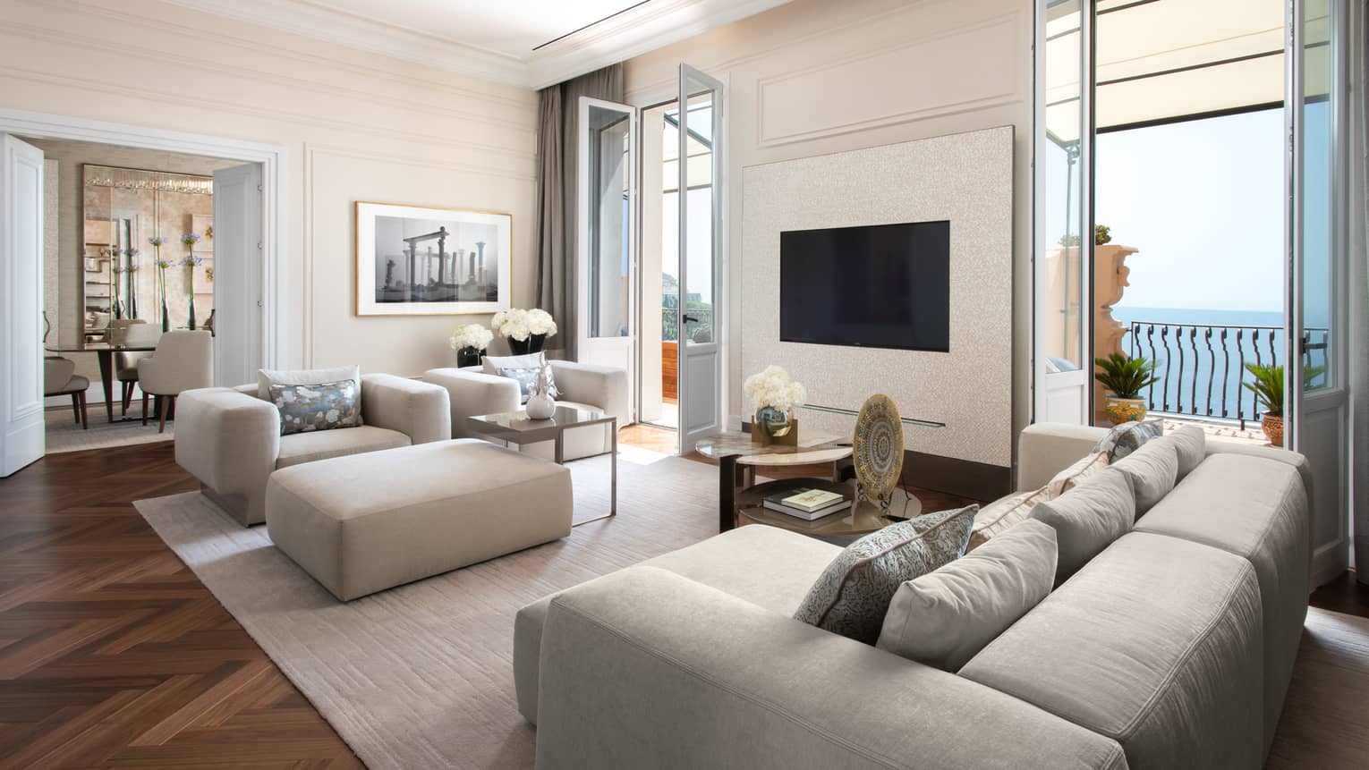 Living room with grey sofa, arm chair and ottoman, two doors opening to sea-view terrace