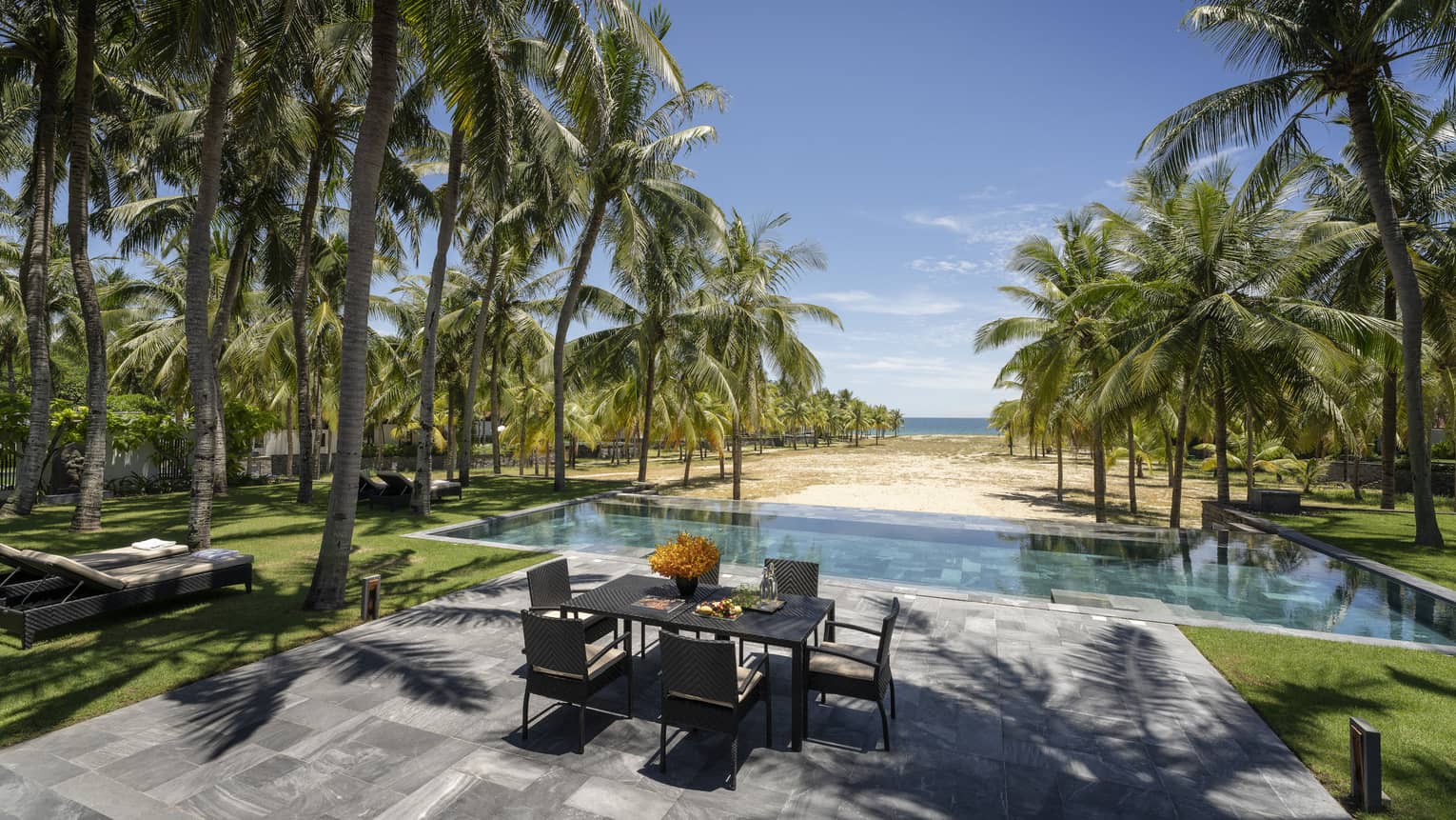Three-Bedroom Pool Villa pool area with dining table, lounge chairs, palm trees, ocean views