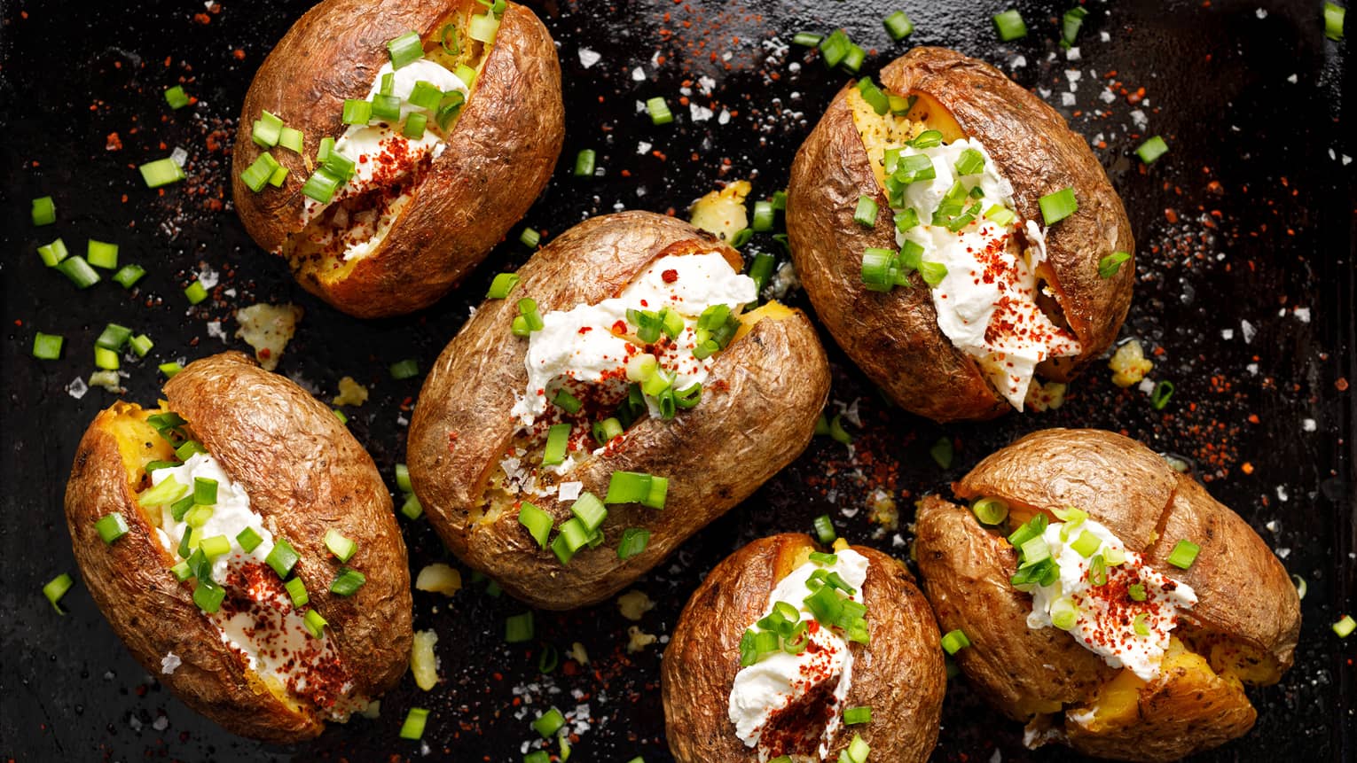 Six baked potatoes filled with cream cheese and sprinkled with green onions, pepper on black table