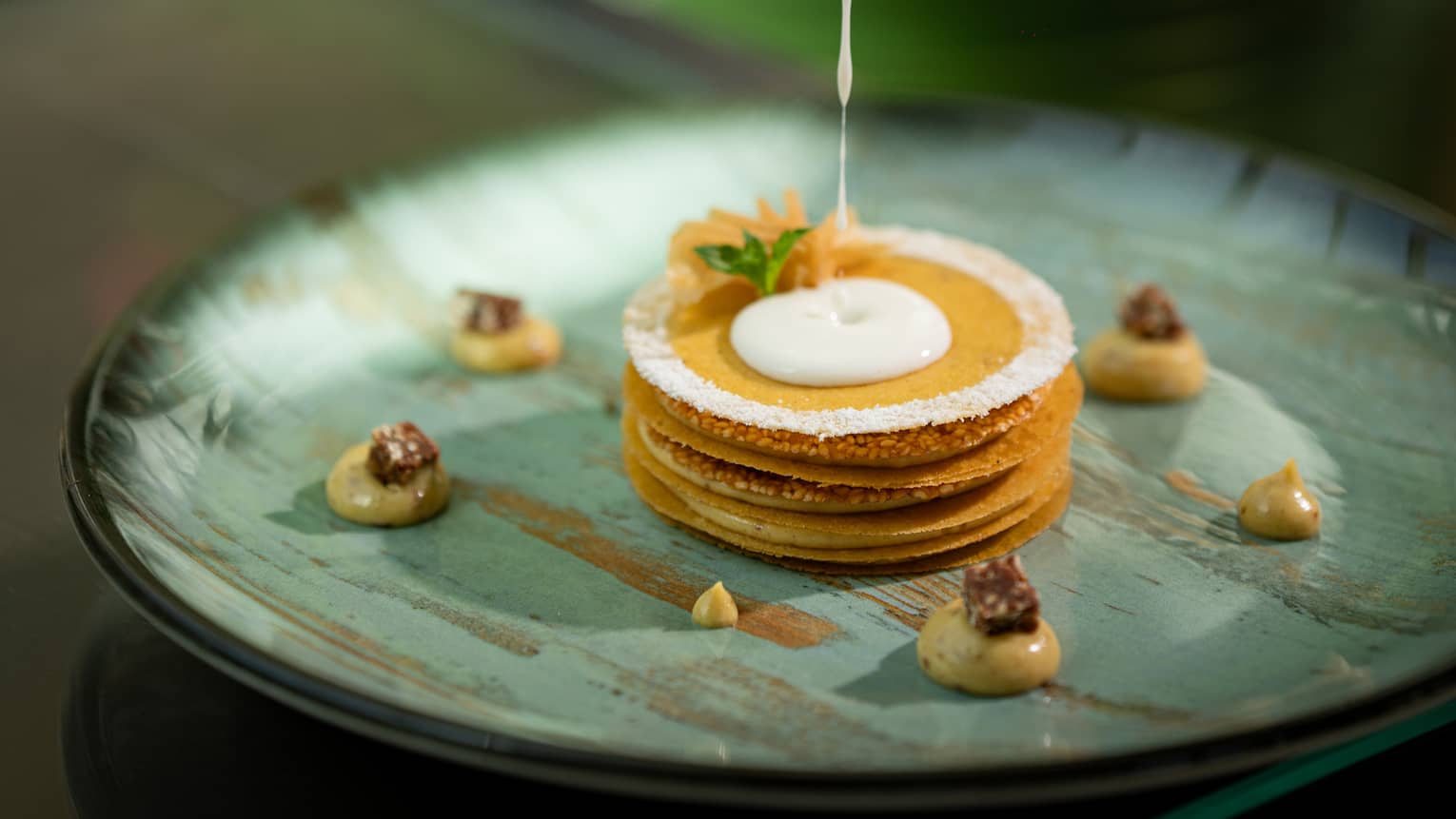 Stack of caramelized puff pastries with white cream being poured over
