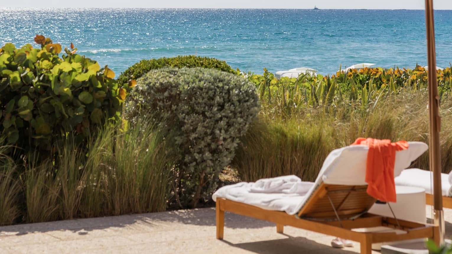 Two lounge chairs set under a pink umbrella sit under a tree with with ocean in the near distance