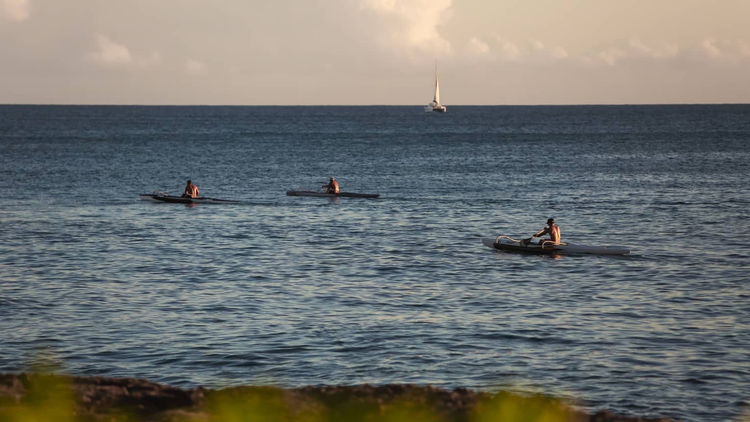 Three kayakers in the ocean with a sailboat in the background