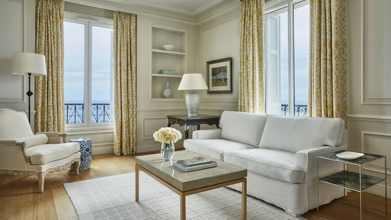 Modern white sofa, armchair, rug, table with books, flowers, corner windows