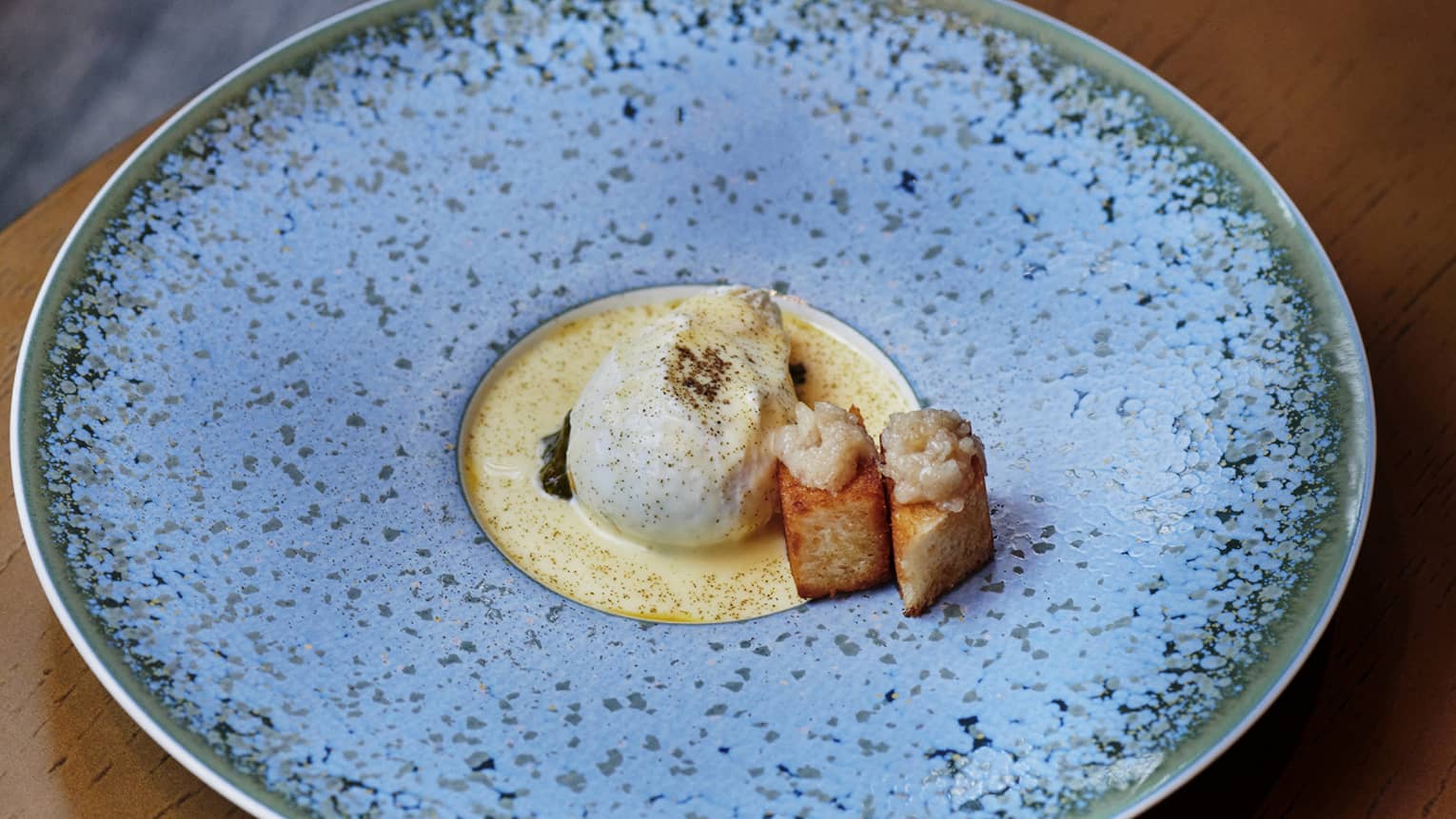 Badaboum signature dish with poached egg, caviar and toasted bread cubes on a textured blue plate