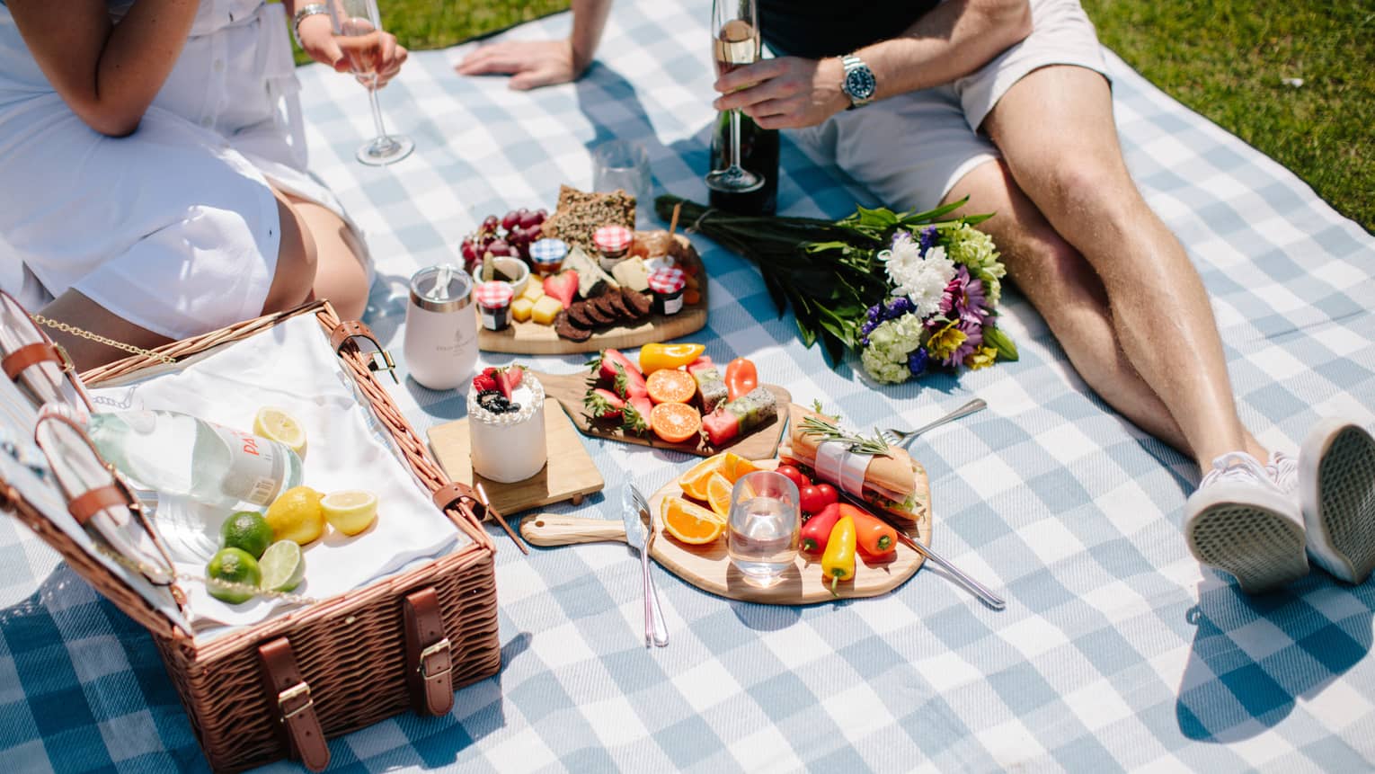 Two people enjoying a large picnic in a park during a sunny day.