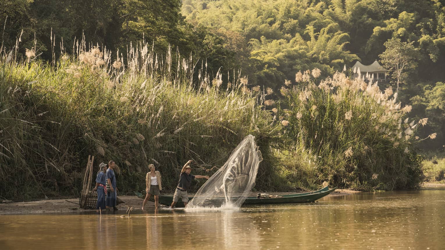 Man throws traditional Thai fishing net from boat into river during group activity