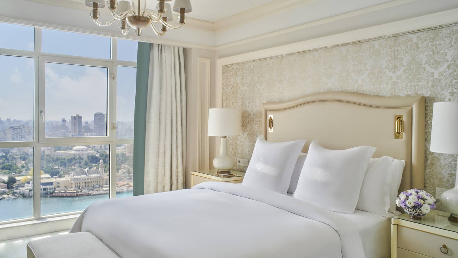 Guest bedroom with king bed, white linens and cream tufted headboard; floor-to-ceiling window with views of the River Nile