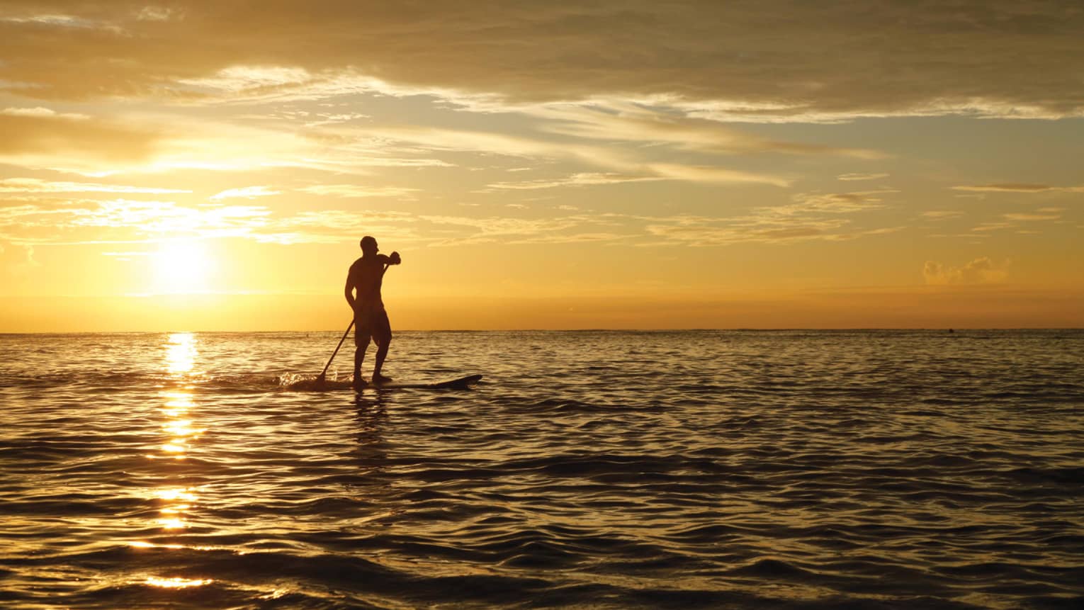 Silhouette of person with paddle on stand-up paddleboard on ocean, orange sunset