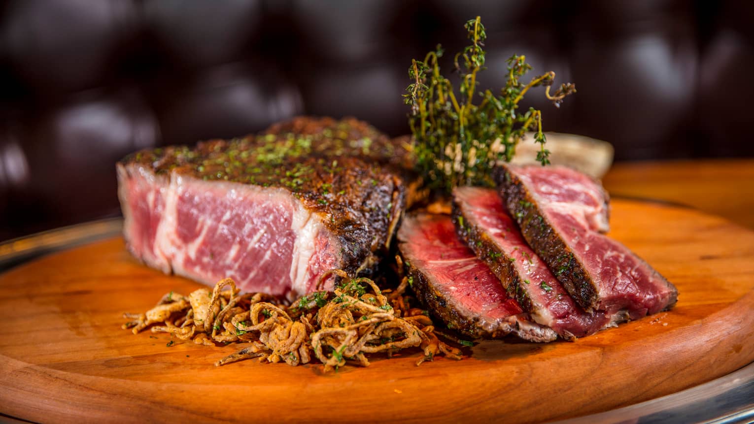 Close-up of Butcher & Still Signature Tomahawk Chop raw steak on wood butcher's block with crispy onion, herbs