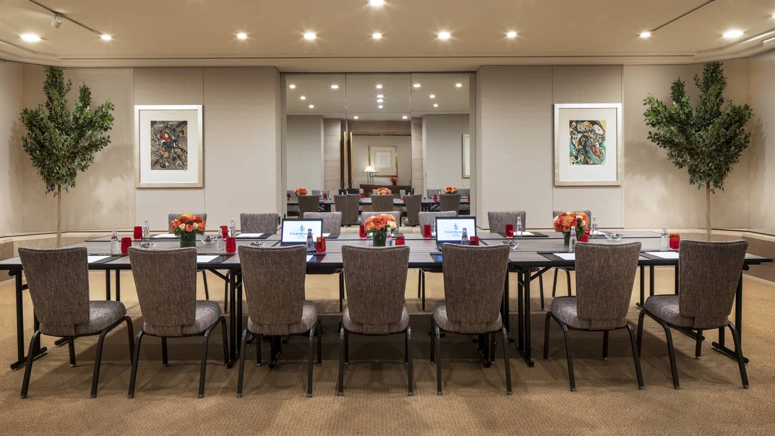 A long rectangular boardroom table is set with a black folder, white paper, pen and clear bottles filled with a red soda. 