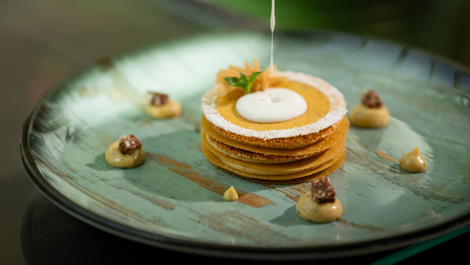 Stack of caramelized puff pastries with white cream being poured over